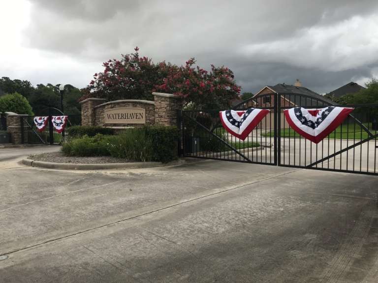 Gated neighborhood entrance with patriotic bunting on brick columns