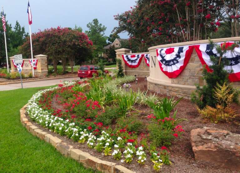 Brick neighborhood entrance wall lined with patriotic bunting fans and US flags above a flower bed