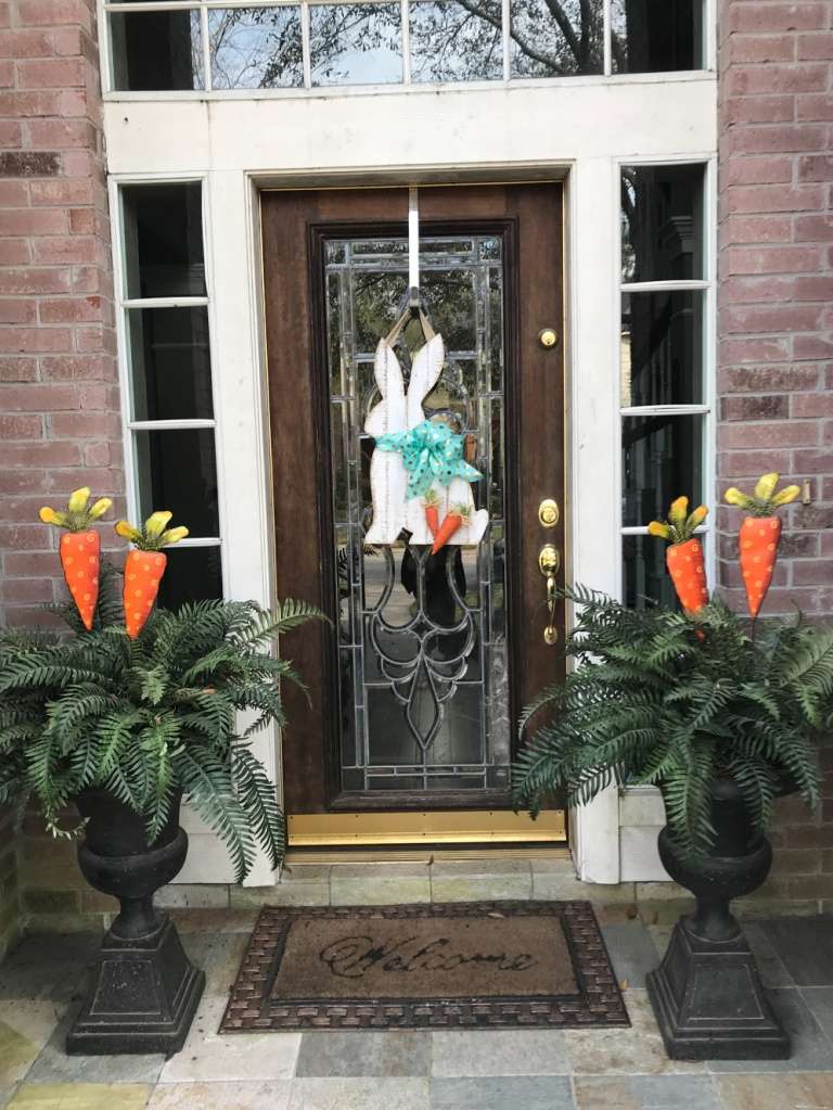 Front door decorated for Easter with a bunny wreath and carrot-topped planters