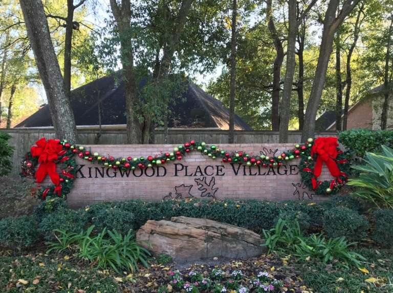 Kingwood Place Village entrance sign decorated with Christmas garland and red bows