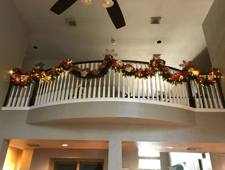 Upstairs balcony railing wrapped in lit Christmas garland with red bows