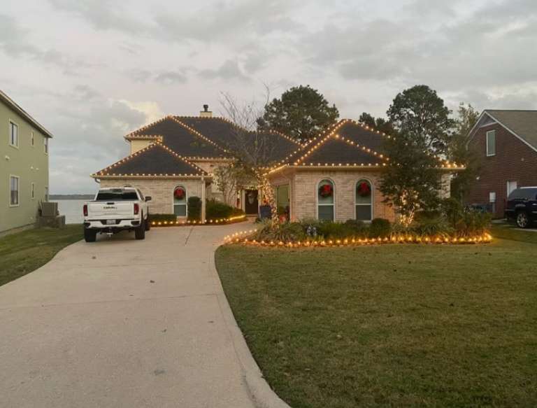 Single-story brick home with Christmas lights installed along the roofline, seen in daylight
